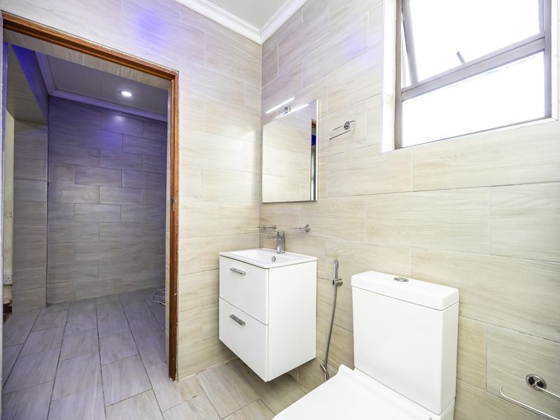 A modern, well-maintained bathroom featuring neutral wall tiles, a wall-mounted vanity with basin, and a contemporary toilet suite.