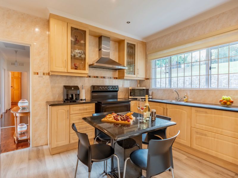 A well-maintained kitchen featuring light wood cabinetry, dark granite countertops, a stainless steel extractor fan, and a tiled backsplash with a functional layout.