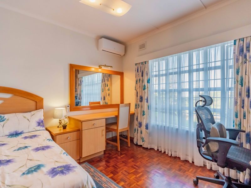 A well-maintained bedroom featuring warm parquet flooring, a built-in vanity unit, and a split-system air conditioner for climate control.