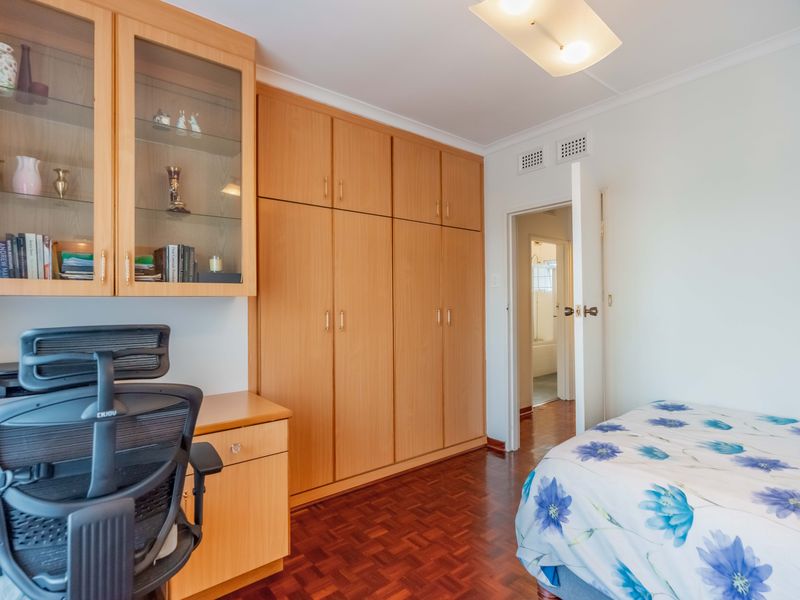 A bedroom featuring parquet flooring, extensive built-in wooden cabinetry, and a built-in desk, with direct access to an adjoining bathroom.