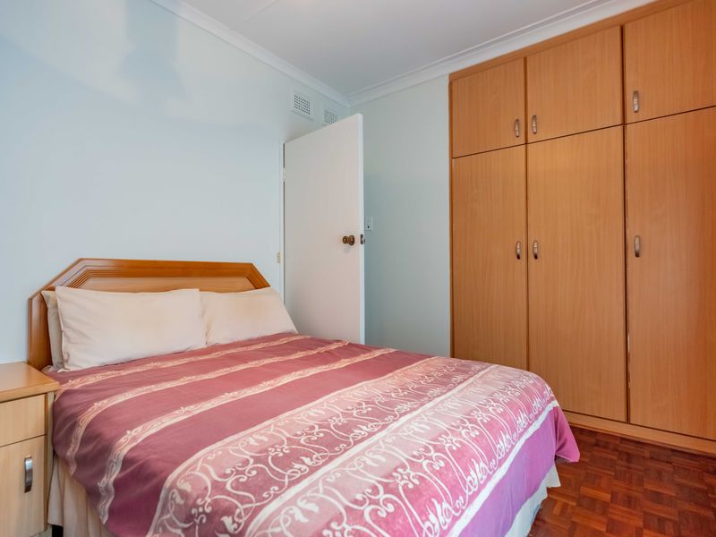 A bedroom featuring parquet flooring and a large built-in wooden wardrobe with ample storage space.