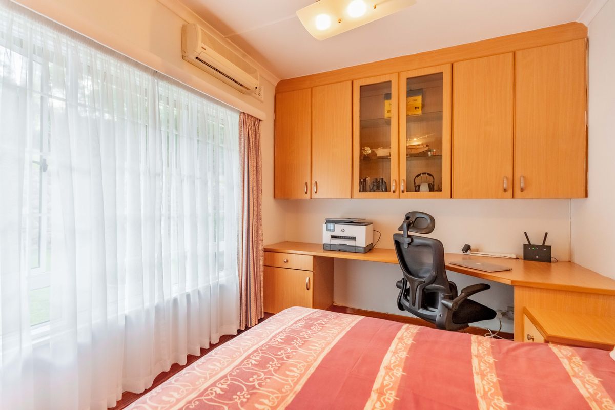 Bedroom featuring built-in wooden cabinetry, a dedicated desk area, and a wall-mounted air conditioning unit.
