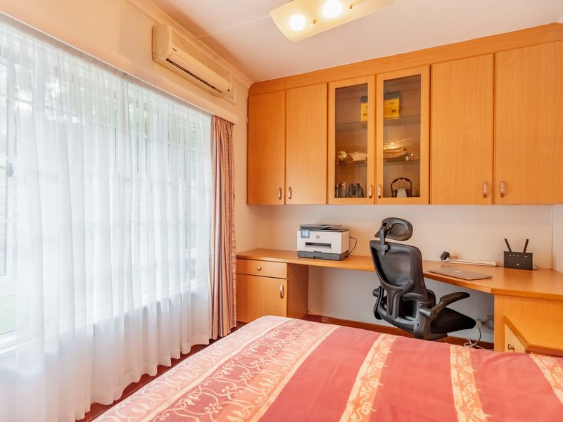 Bedroom featuring built-in wooden cabinetry, a dedicated desk area, and a wall-mounted air conditioning unit.