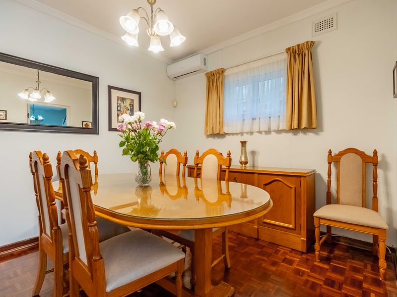 A dining room featuring classic parquet flooring, a wall-mounted split system air conditioner, and a central ceiling light fixture.