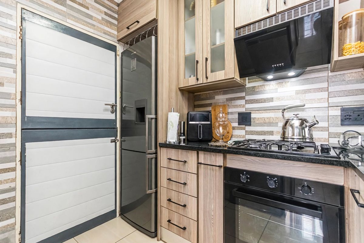 Modern kitchen featuring wood-finish cabinetry, granite countertops, a gas hob with extractor fan, and a distinctive stable-style door.