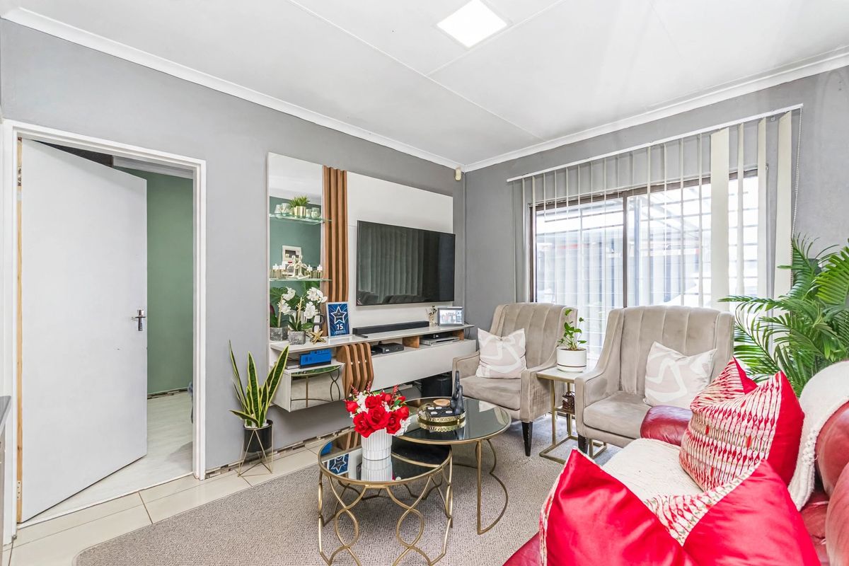 A comfortable living room featuring a built-in media unit, tiled flooring, and a sliding glass door with vertical blinds providing natural light.