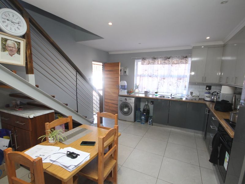Open-plan kitchen and living area featuring modern grey cabinetry, tiled flooring, and a staircase with a contemporary stainless steel balustrade.