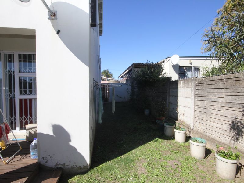 A side view of the townhouse exterior featuring a small lawn, precast concrete boundary wall, and access to the rear patio area.