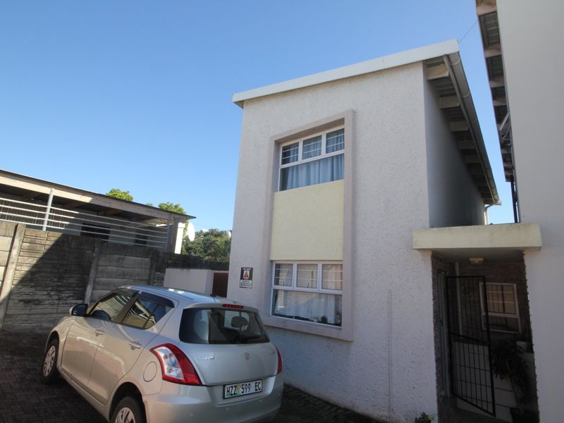 Front exterior view of a townhouse featuring a paved driveway, security gate, and standard aluminium window frames.