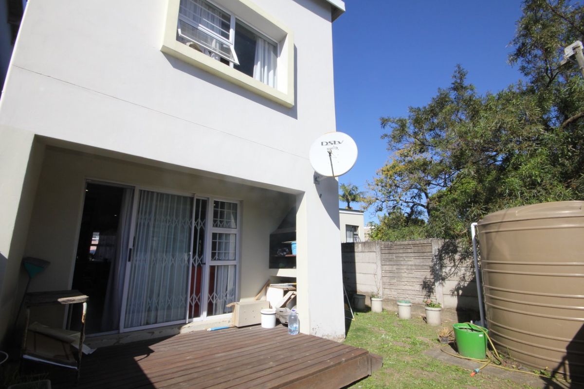 Rear exterior view of the townhouse featuring a wooden deck, built-in braai area, sliding door access, and a water storage tank in the garden.