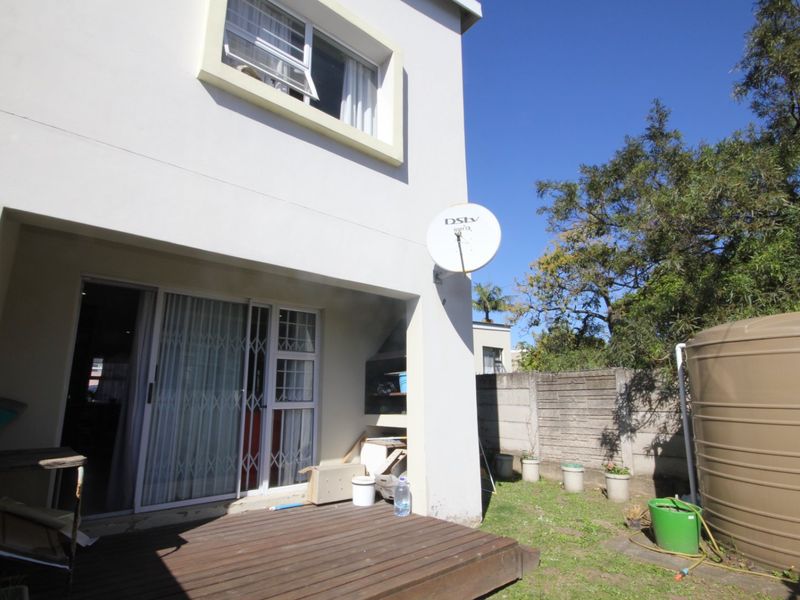 Rear exterior view of the townhouse featuring a wooden deck, built-in braai area, sliding door access, and a water storage tank in the garden.