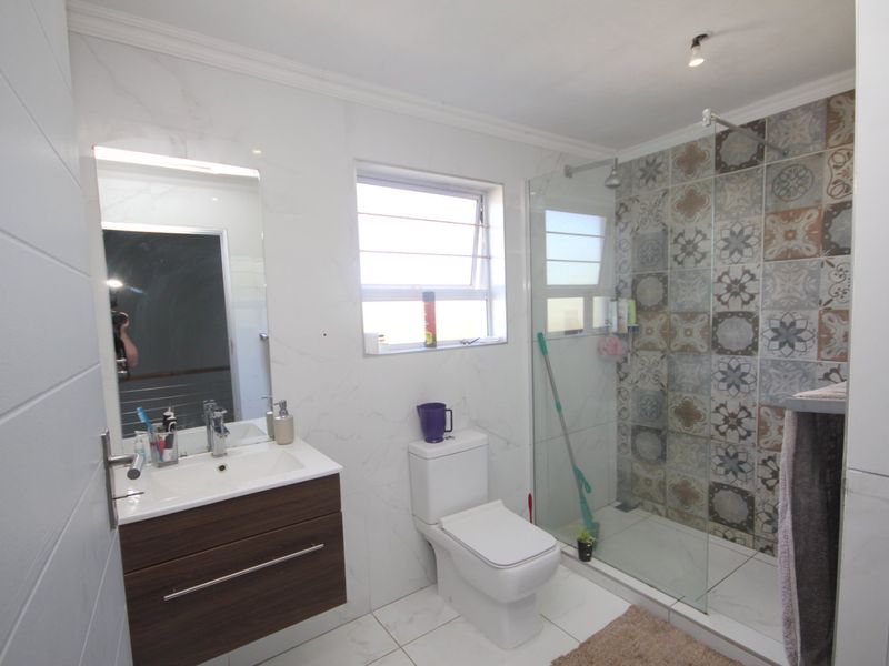 Modern bathroom featuring a floating vanity, walk-in shower with decorative patterned tiling, and neutral floor tiles.