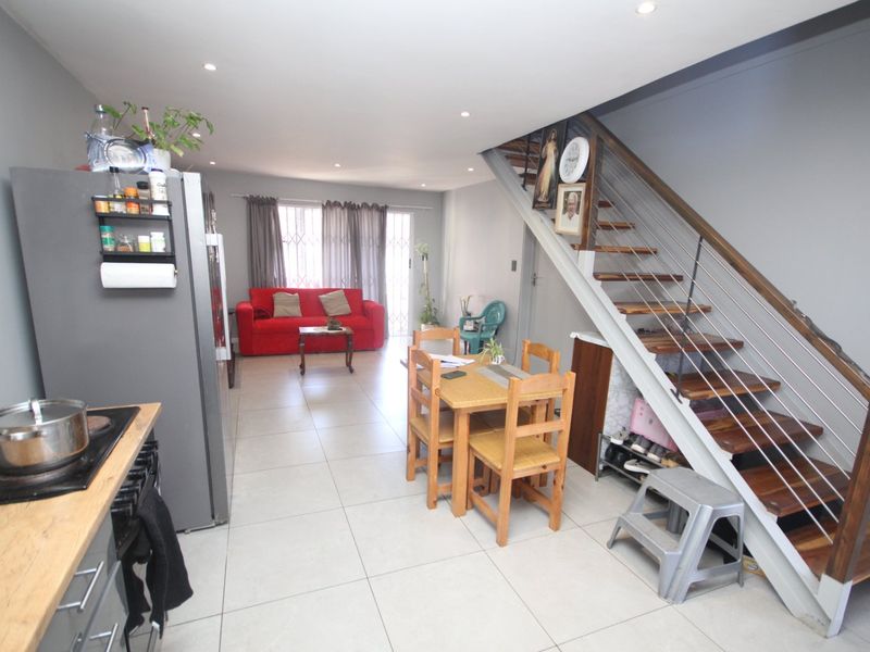 Open-plan living area featuring tiled floors, recessed lighting, and a modern staircase with timber treads, seamlessly connecting the kitchen and lounge space.