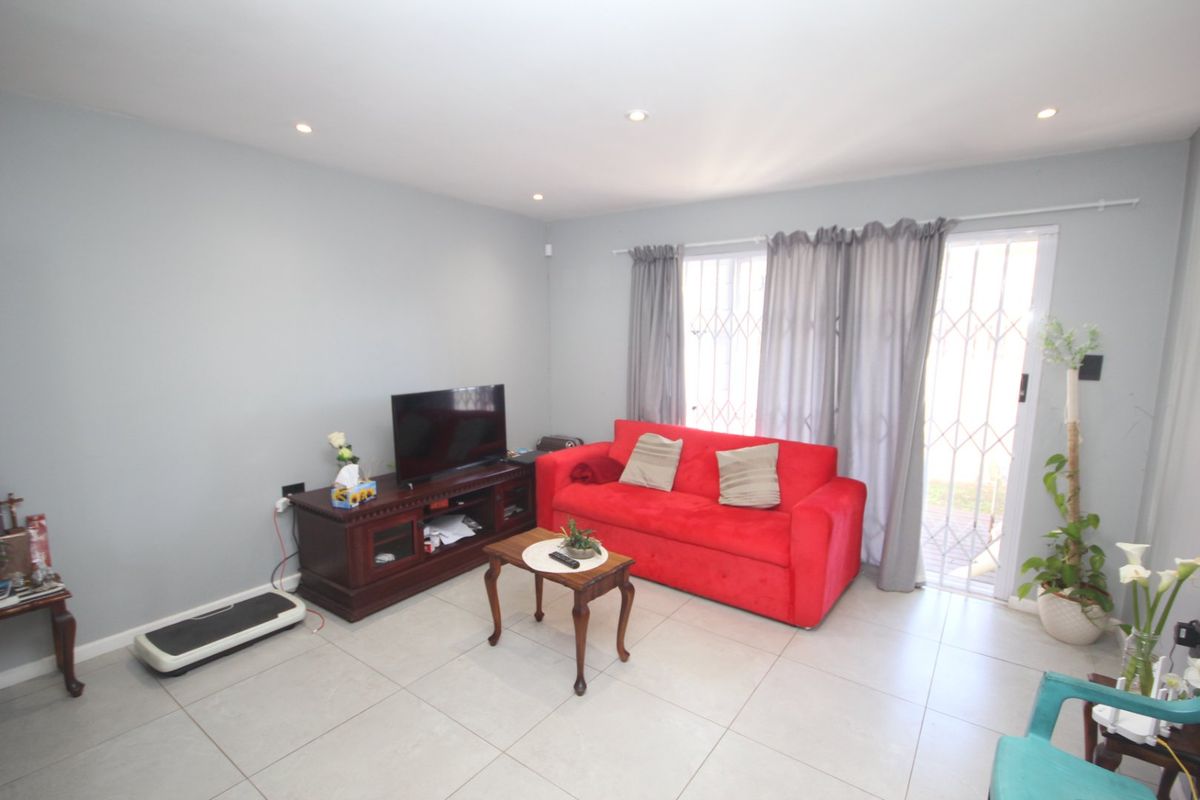 A bright living room featuring neutral tiled flooring, recessed downlighting, and a sliding glass door with an integrated security gate leading to the exterior.