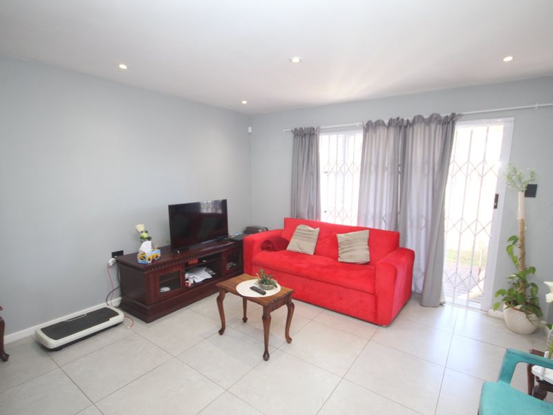 A bright living room featuring neutral tiled flooring, recessed downlighting, and a sliding glass door with an integrated security gate leading to the exterior.