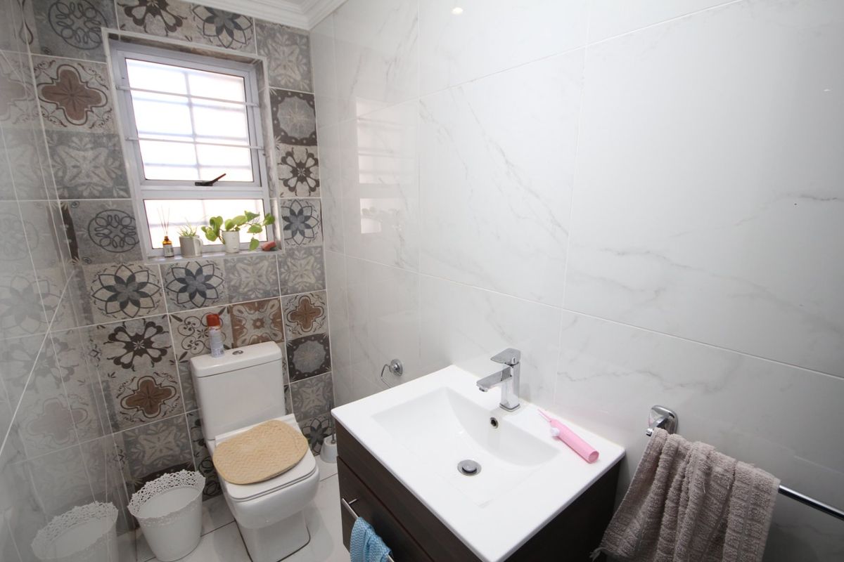 A modern bathroom featuring a vanity cabinet with a basin, a toilet, and a combination of patterned and marble-look wall tiles.
