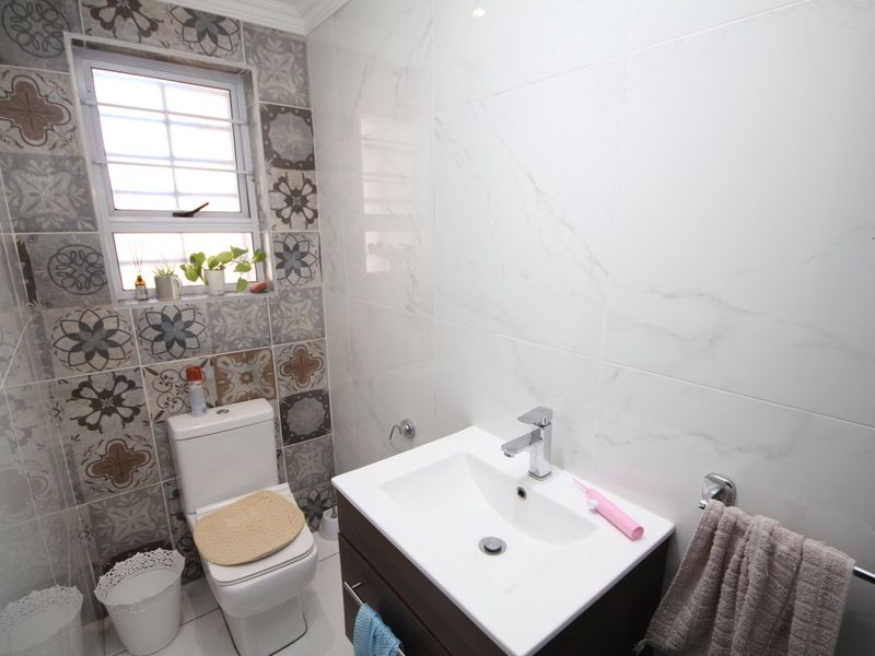 A modern bathroom featuring a vanity cabinet with a basin, a toilet, and a combination of patterned and marble-look wall tiles.