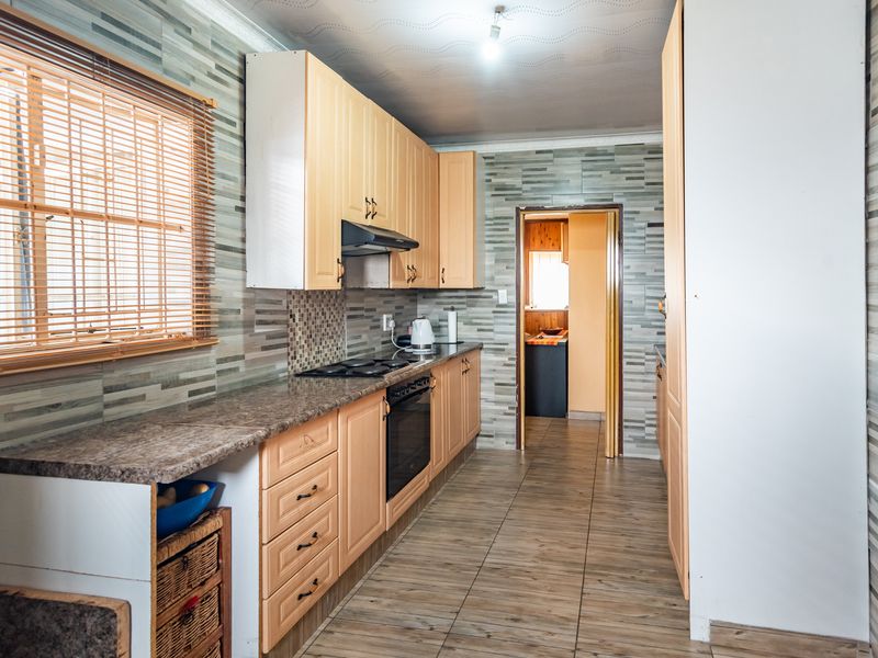 A functional kitchen featuring light wood cabinetry, laminate countertops, a built-in oven with hob, and tiled finishes throughout.