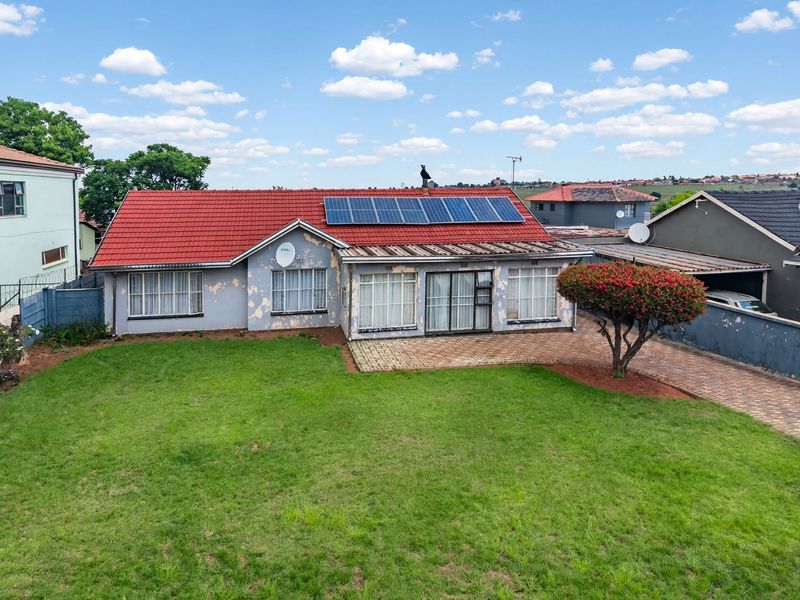 Rear view of a detached house featuring a tiled roof with solar panels, a paved patio area, and a spacious lawn.