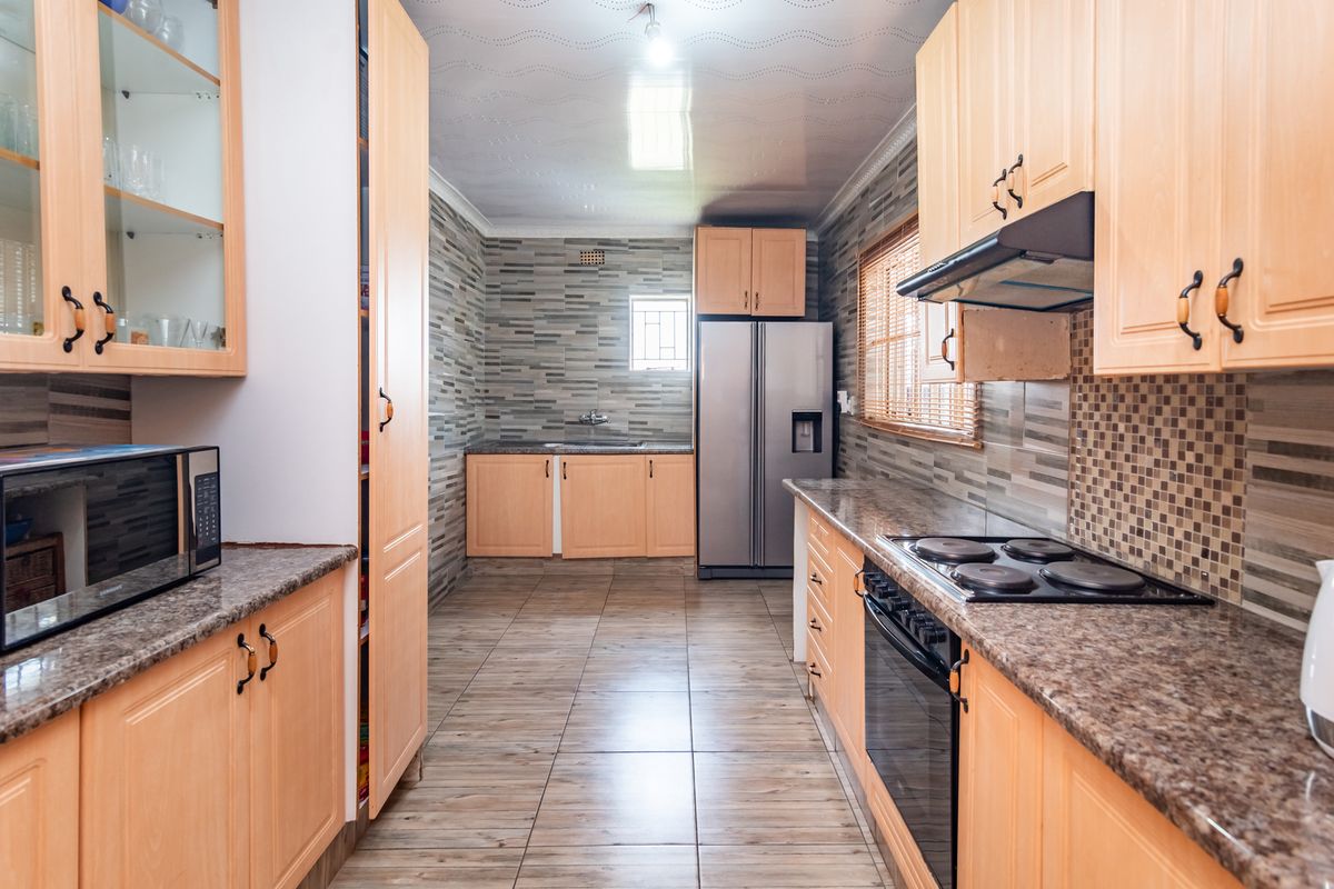 A functional kitchen featuring light wood cabinetry, granite countertops, a built-in oven with hob, and tiled finishes throughout.