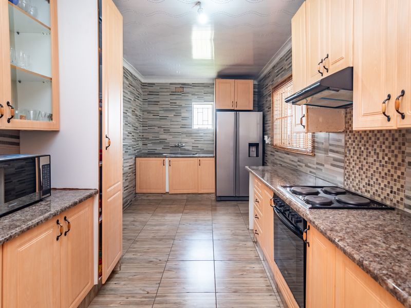A functional kitchen featuring light wood cabinetry, granite countertops, a built-in oven with hob, and tiled finishes throughout.