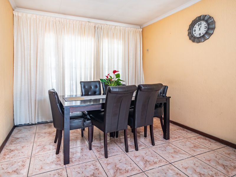 A functional dining room featuring tiled flooring and large windows with floor-to-ceiling curtains, providing a bright and neutral space for family meals.