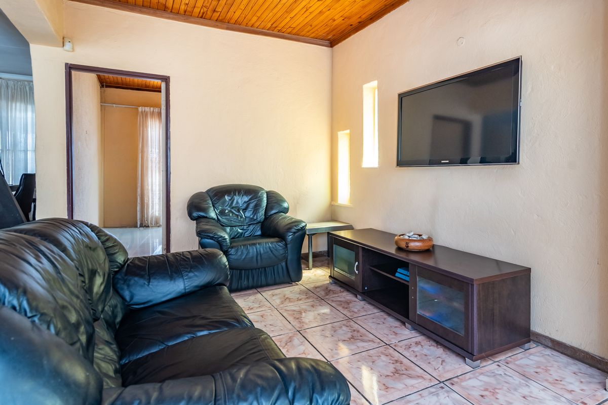 A living room featuring a timber-clad ceiling, tiled flooring, and built-in wall niches, providing a functional space with potential for cosmetic updates.