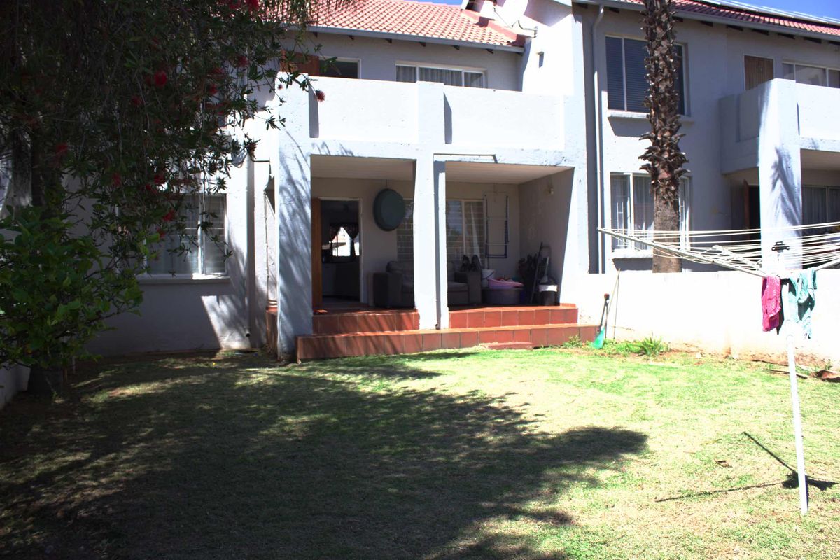 Rear view of the townhouse featuring a covered patio with terracotta steps, a private garden, and a tiled roof.