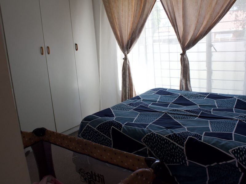 A bedroom featuring built-in cupboards and security bars on the window, providing a functional and secure living space.