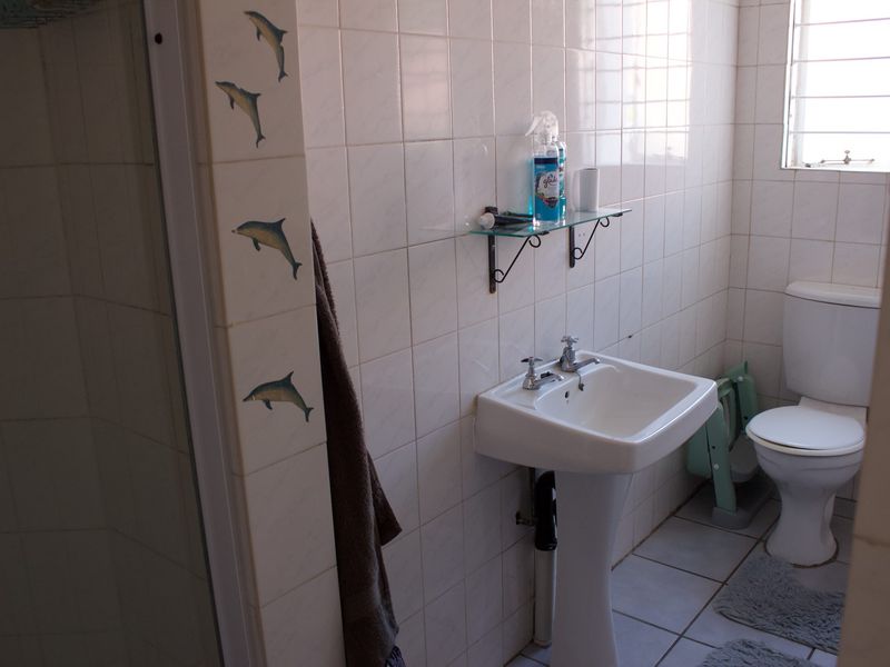 A functional bathroom featuring a pedestal basin, toilet, and shower enclosure with white ceramic wall and floor tiles.
