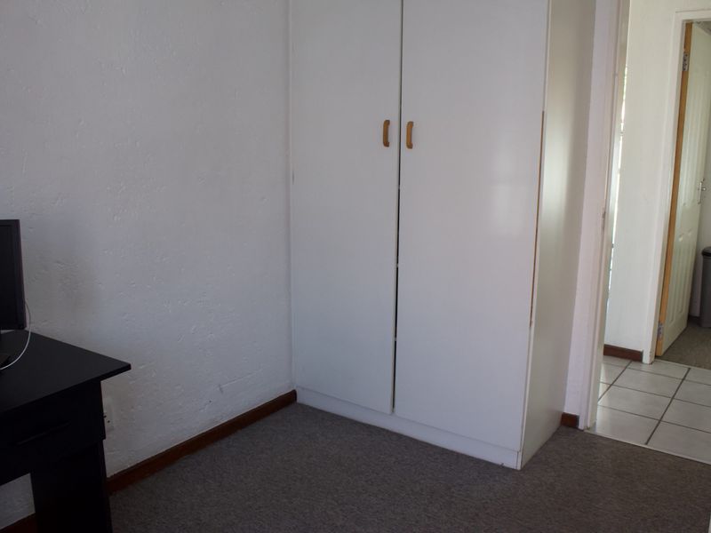 A bedroom featuring a built-in wardrobe with white cabinetry and carpeted flooring, leading into an adjacent tiled hallway.