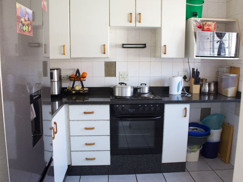 Compact kitchen featuring white cabinetry, dark granite countertops, built-in oven and hob, and tiled backsplash.