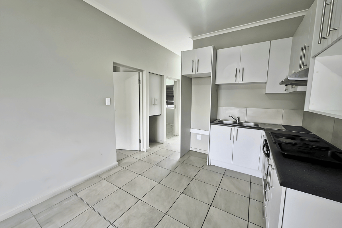 A clean, modern kitchen featuring white cabinetry, dark countertops, built-in hob with extractor, and neutral tiled flooring in an open-plan layout.