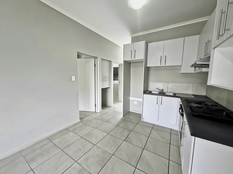 A clean, modern kitchen featuring white cabinetry, dark countertops, built-in hob with extractor, and neutral tiled flooring in an open-plan layout.