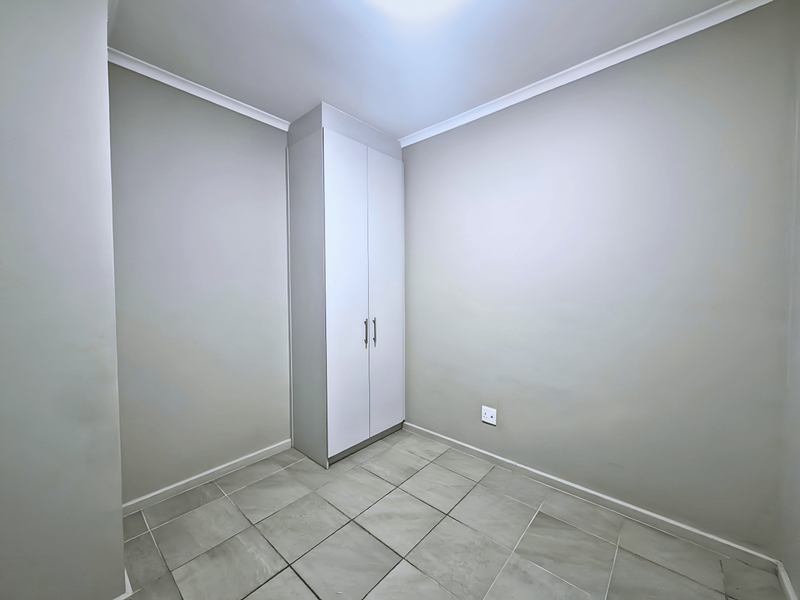 A clean, empty bedroom featuring neutral wall paint, tiled flooring, and a built-in wardrobe with white doors.