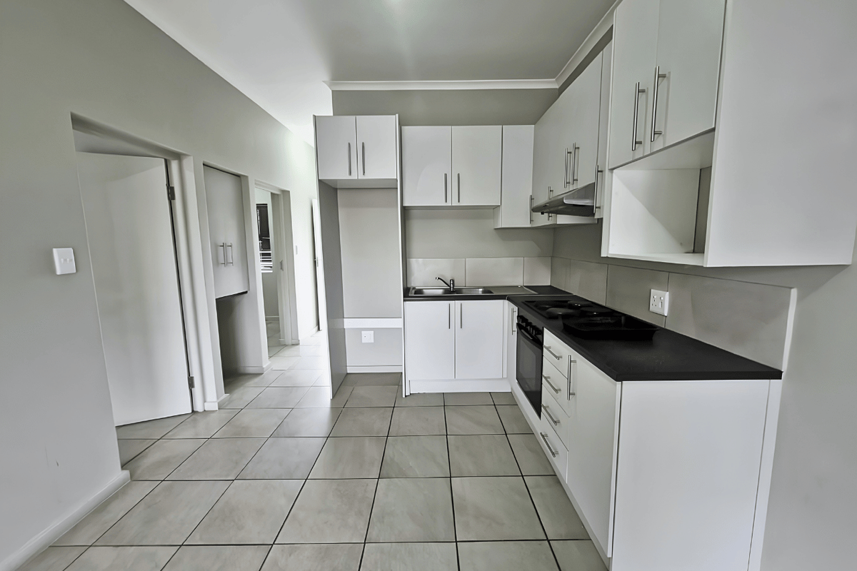 A clean, modern kitchen featuring white cabinetry, dark countertops, built-in oven, hob, extractor fan, and neutral tiled flooring.