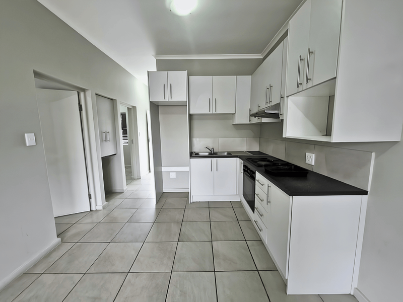 A clean, modern kitchen featuring white cabinetry, dark countertops, built-in oven, hob, extractor fan, and neutral tiled flooring.