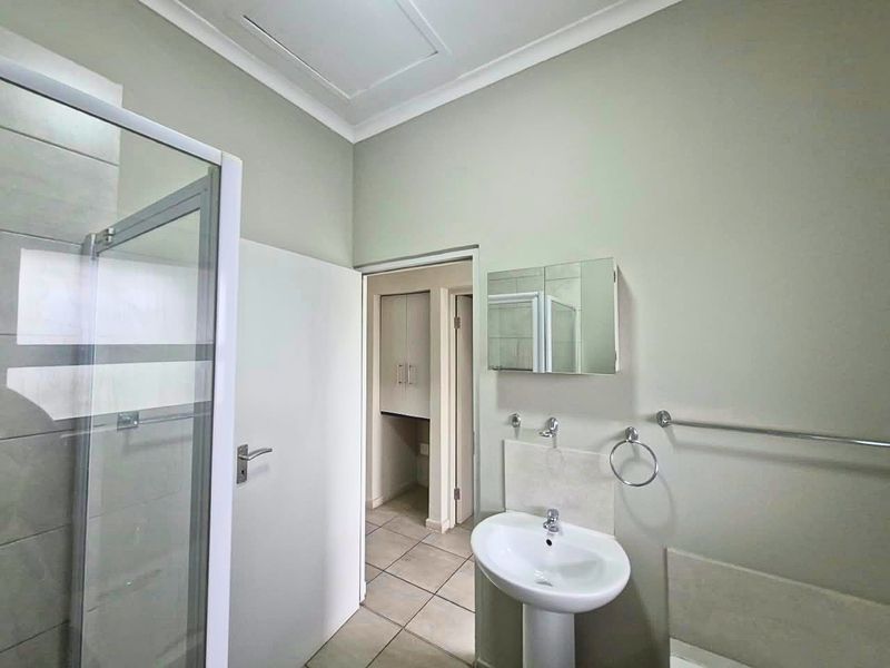 A clean and functional bathroom featuring a pedestal sink, glass shower enclosure, tiled flooring, and additional built-in storage space.