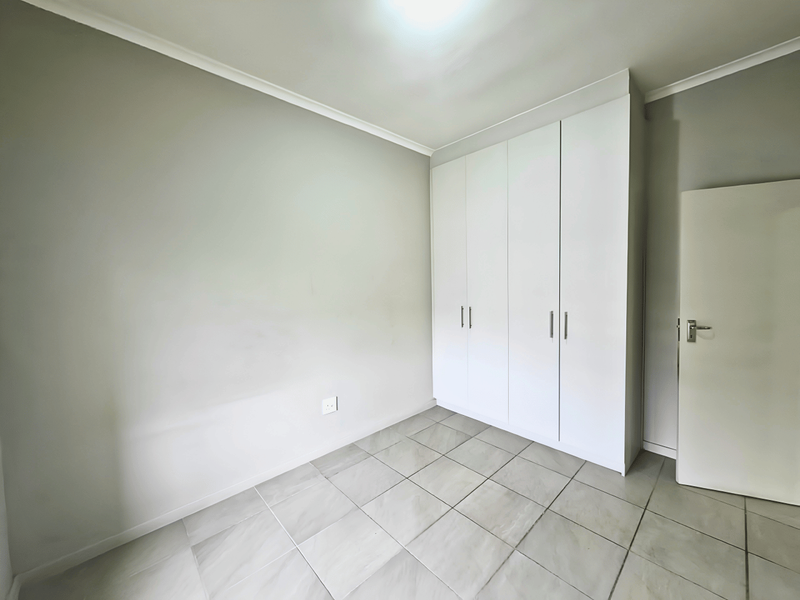 A clean, empty bedroom featuring neutral walls, tiled flooring, and white built-in cupboards, offering a versatile space ready for personalization.