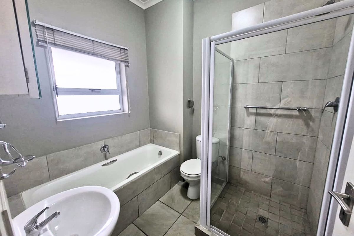 A clean and functional bathroom featuring a separate shower enclosure, built-in bathtub, pedestal basin, and neutral wall and floor tiling.