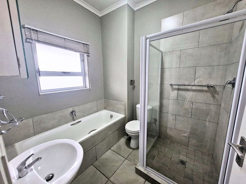 A clean and functional bathroom featuring a separate shower enclosure, built-in bathtub, pedestal basin, and neutral wall and floor tiling.