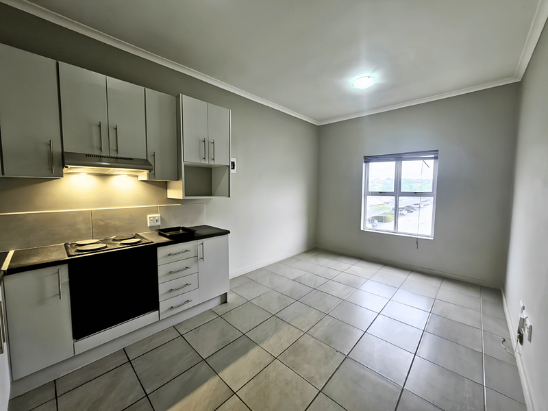 A clean, modern kitchen featuring built-in cabinetry, an electric hob with extractor fan, and neutral tiled flooring in an open-plan layout.