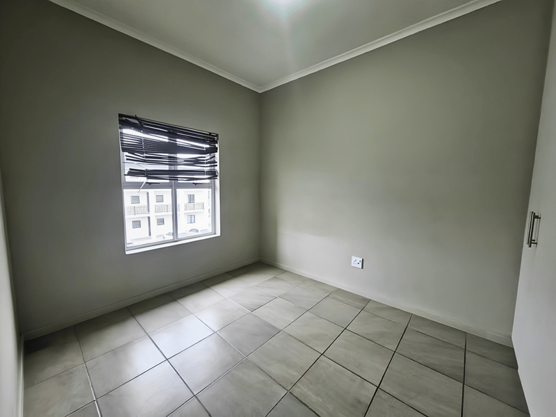 An empty bedroom featuring neutral tiled flooring, a built-in cupboard, and a window fitted with venetian blinds.