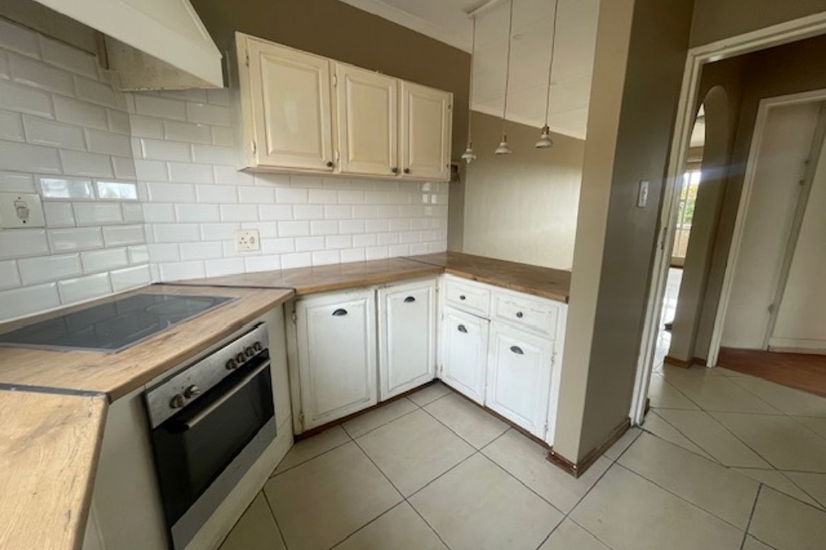 A functional kitchen featuring subway tile backsplash, wooden countertops, built-in oven with hob, and tiled flooring, offering a classic layout ready for modern updates.