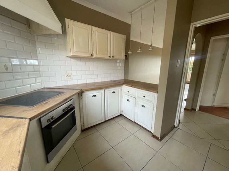 A functional kitchen featuring subway tile backsplash, wooden countertops, built-in oven with hob, and tiled flooring, offering a classic layout ready for modern updates.