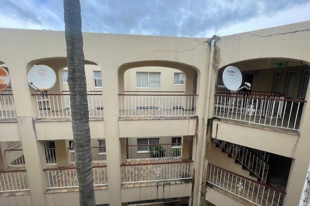 Exterior view of a multi-story flat complex featuring arched balconies, tiled flooring, and metal railings, showing signs of wear and exterior weathering.