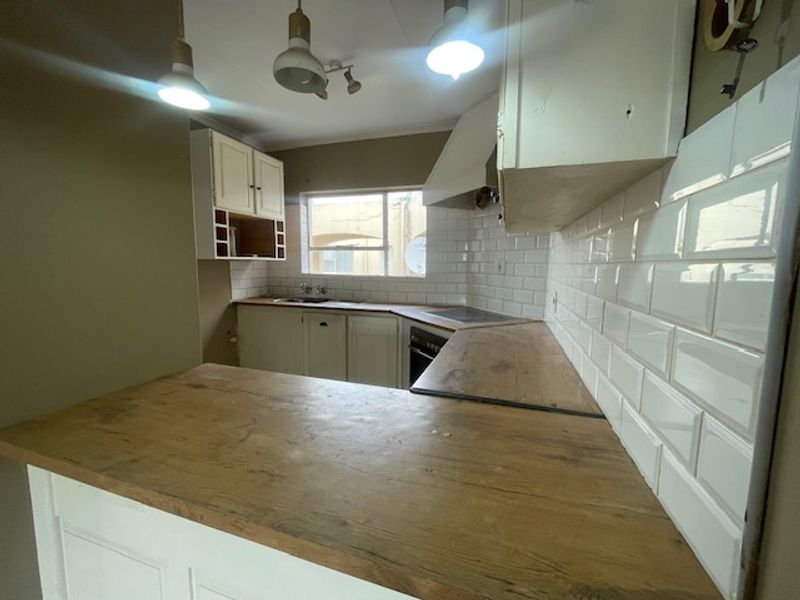 A compact kitchen featuring white cabinetry, subway tile backsplash, and wooden countertops, offering a functional layout ready for modernization.