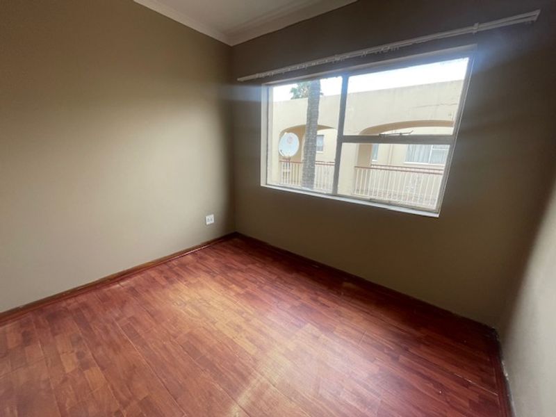 An empty bedroom featuring laminate flooring and a large window, providing a blank canvas for potential interior design and furnishing.