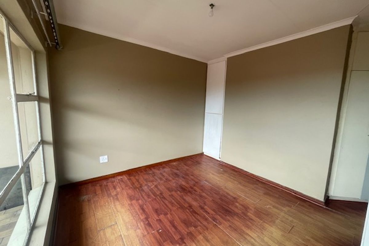 An empty bedroom featuring laminate flooring, built-in cupboard storage, and large aluminium-framed windows allowing for natural light.