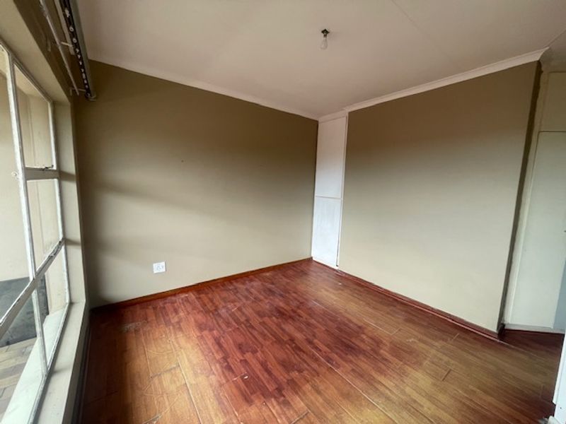 An empty bedroom featuring laminate flooring, built-in cupboard storage, and large aluminium-framed windows allowing for natural light.